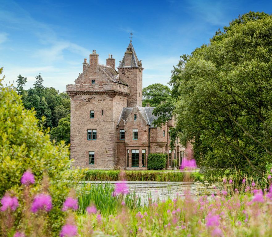 The medieval keep reflected across a wildflower-fringed loch, Guthrie Castle, Forfar, Scotland