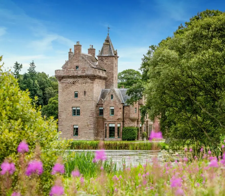 The medieval keep reflected across a wildflower-fringed loch, Guthrie Castle, Forfar, Scotland