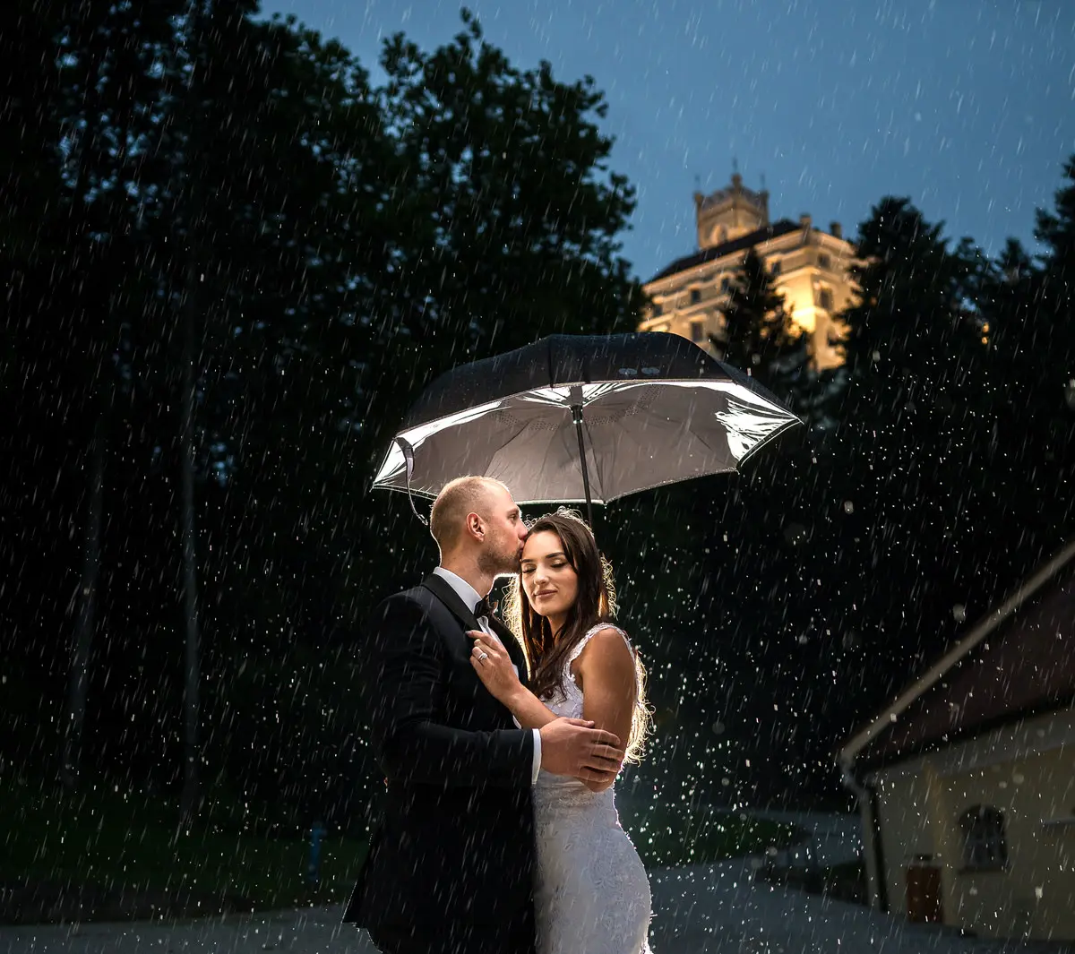 A shared umbrella in the rain, the venue lit up behind them, Reflexion Studio, Dubrovnik, Croatia