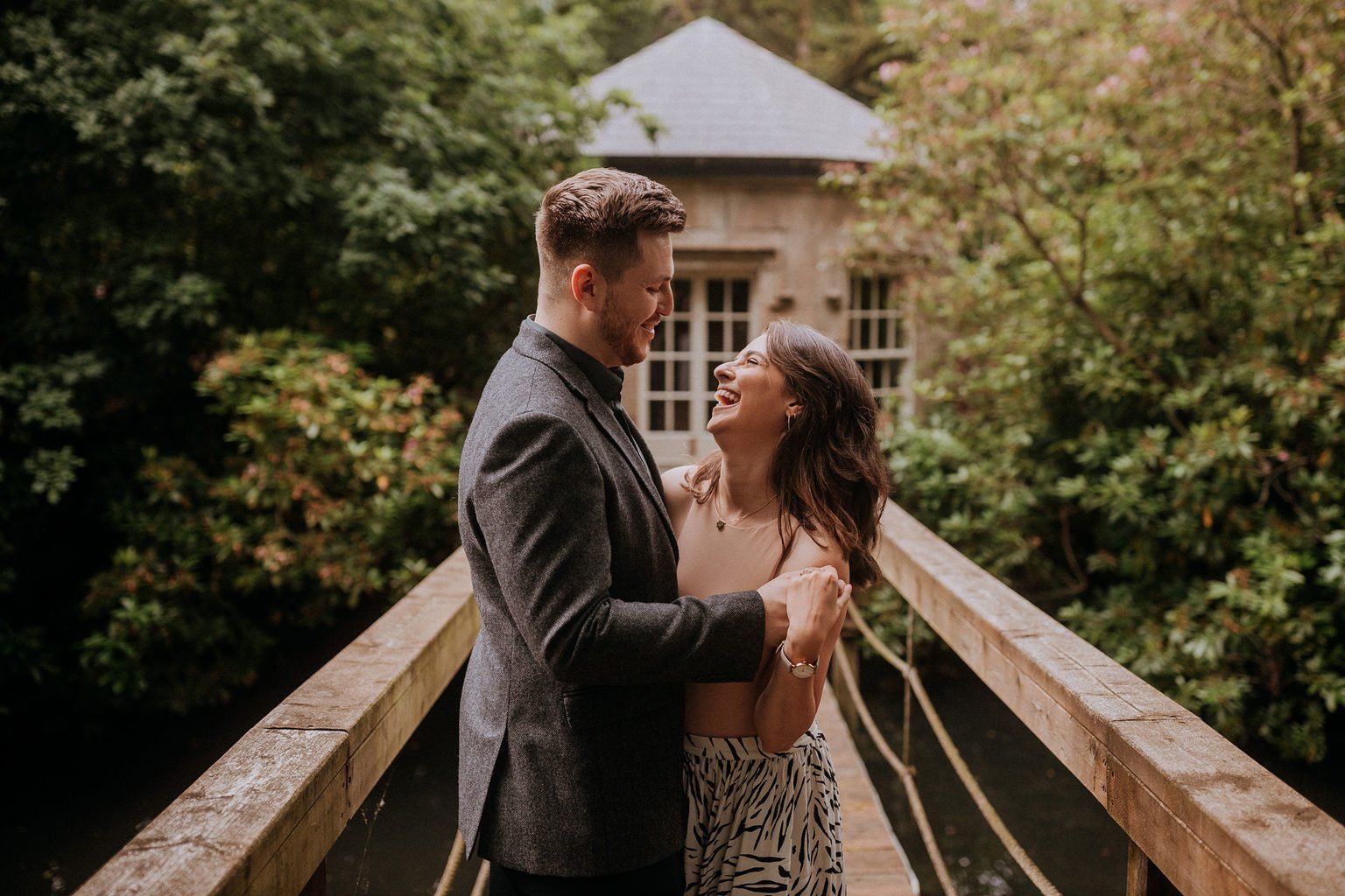 A couple embracing on a wooden footbridge over the estate water, greenery all around