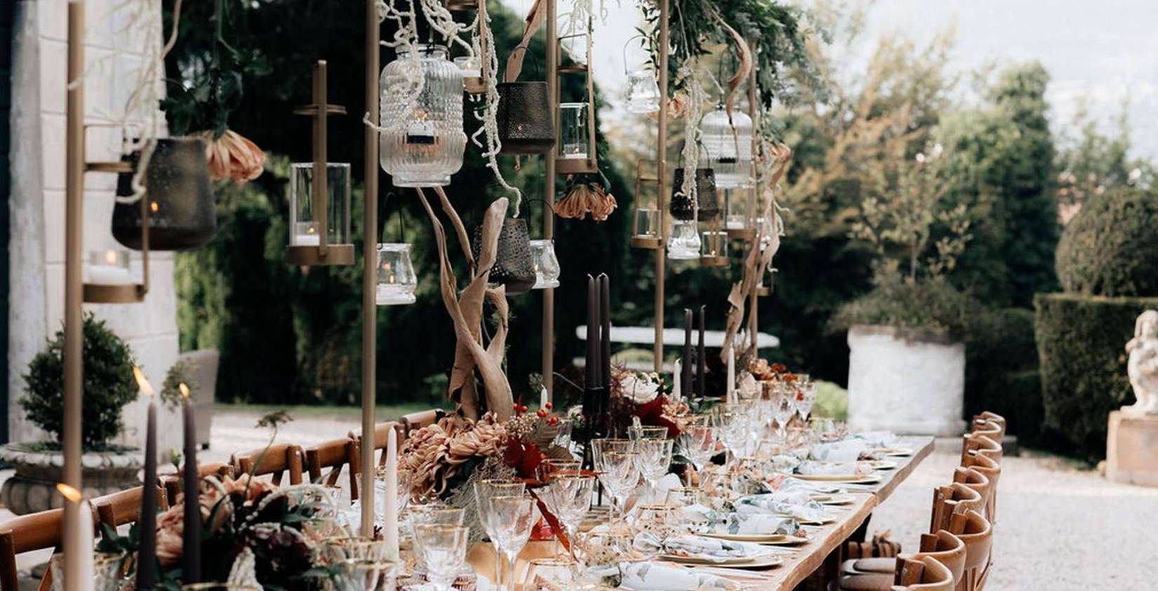 A boho-elegant reception table strung with hanging lanterns, dark autumnal florals and black taper candles