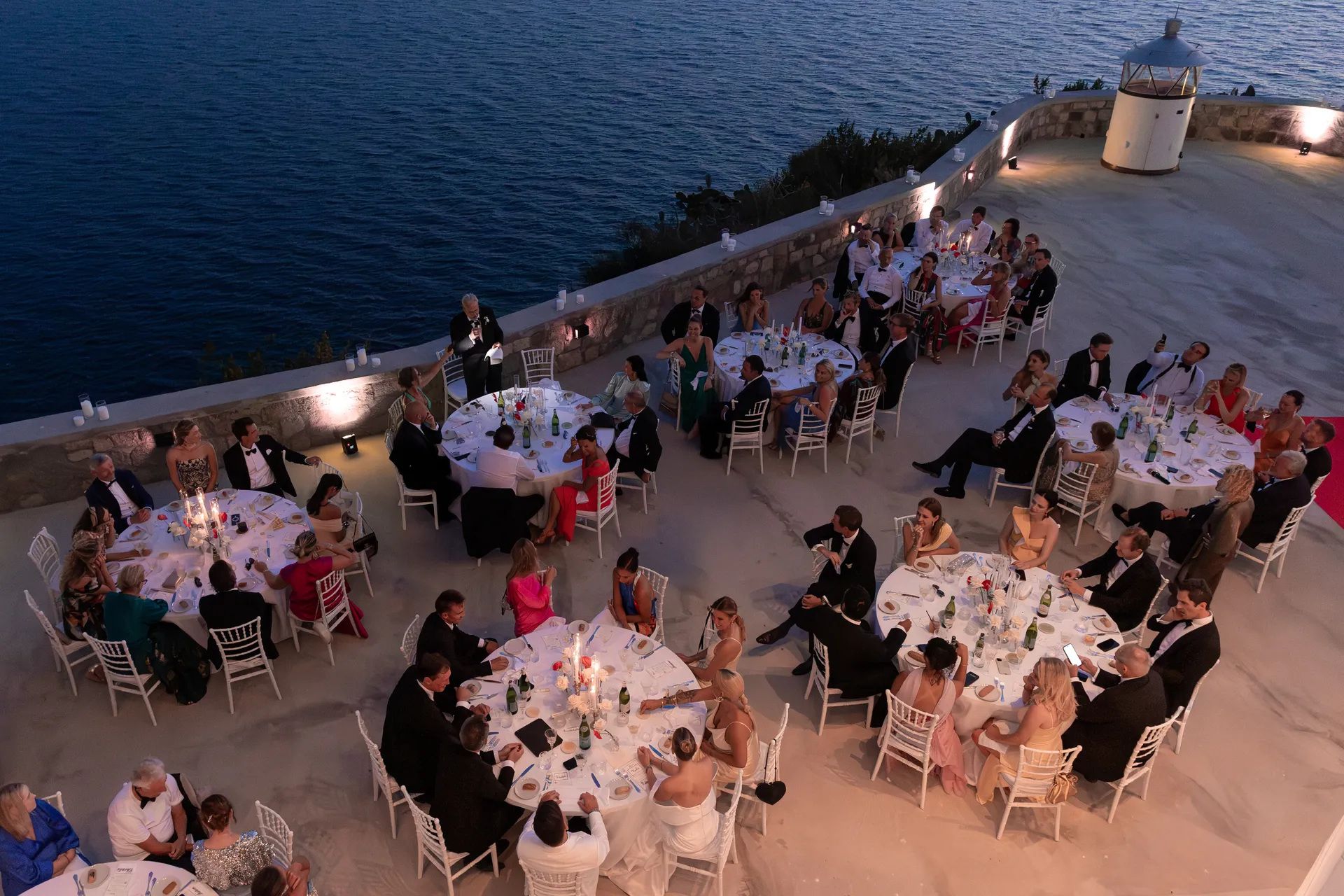 The terrace at night, round tables and the sea beyond the parapet