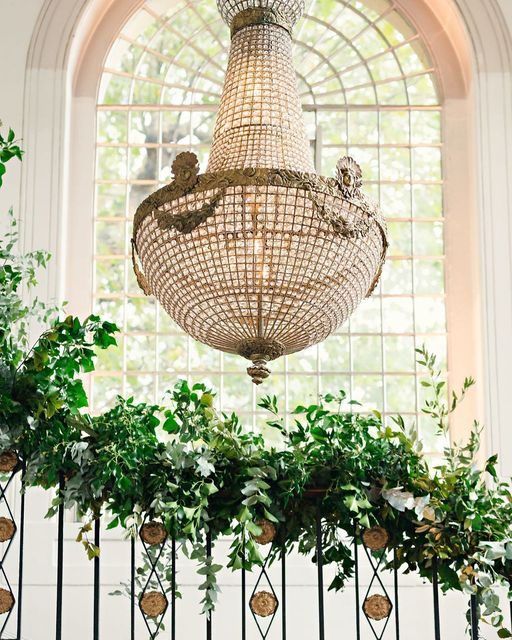 A crystal chandelier and cascading greenery against a tall arched stained-glass window