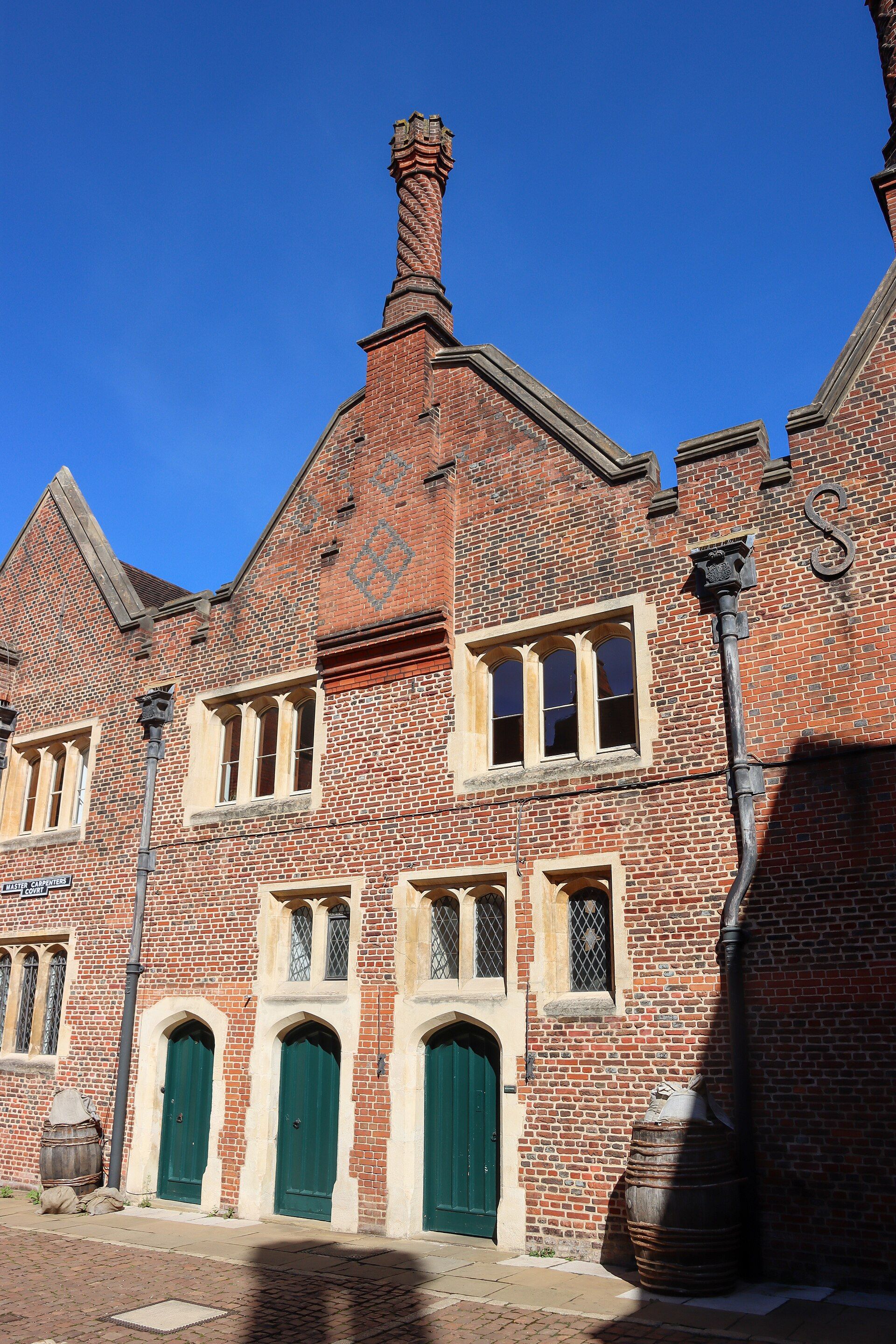 A Tudor gatehouse range of warm brick, chimney and green doors