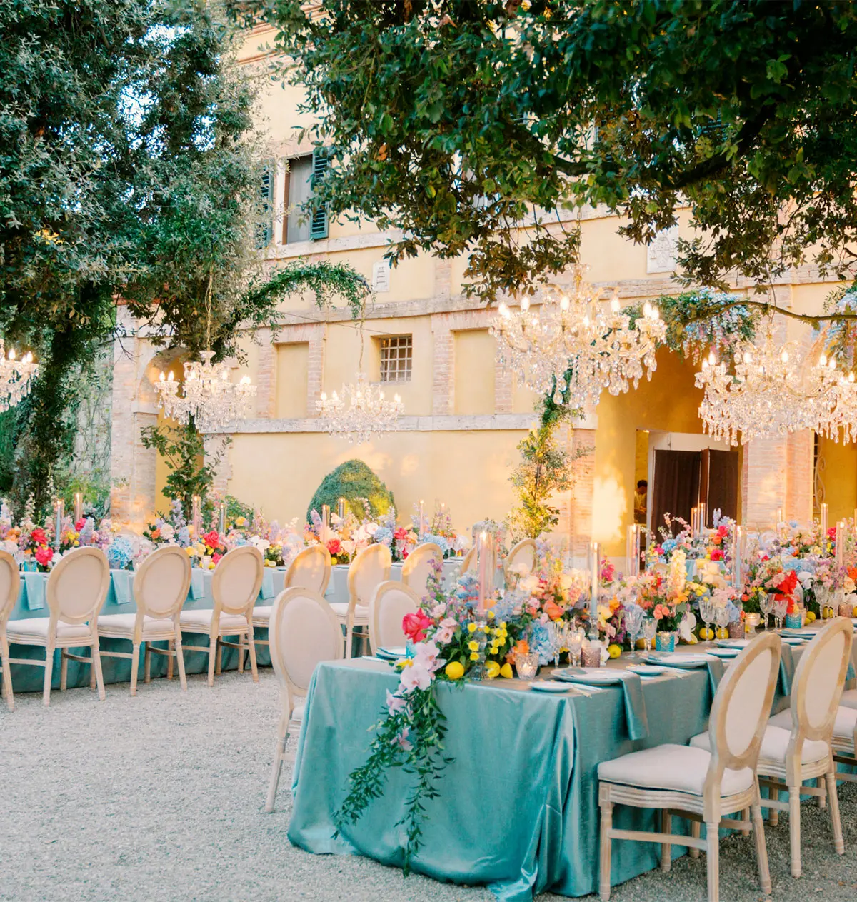 A long table under crystal chandeliers hung from an oak tree, teal linen, Tuscany
