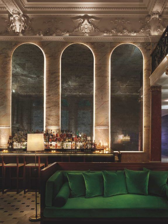 A bar with backlit arched shelving and a green velvet sofa