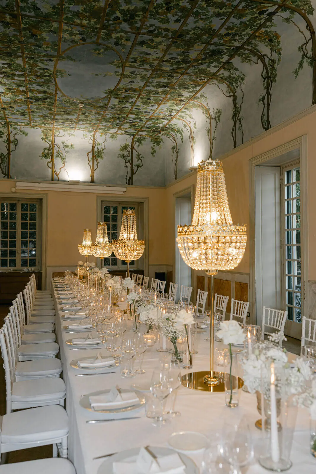 A long table under crystal chandeliers in a frescoed villa room on Lake Como