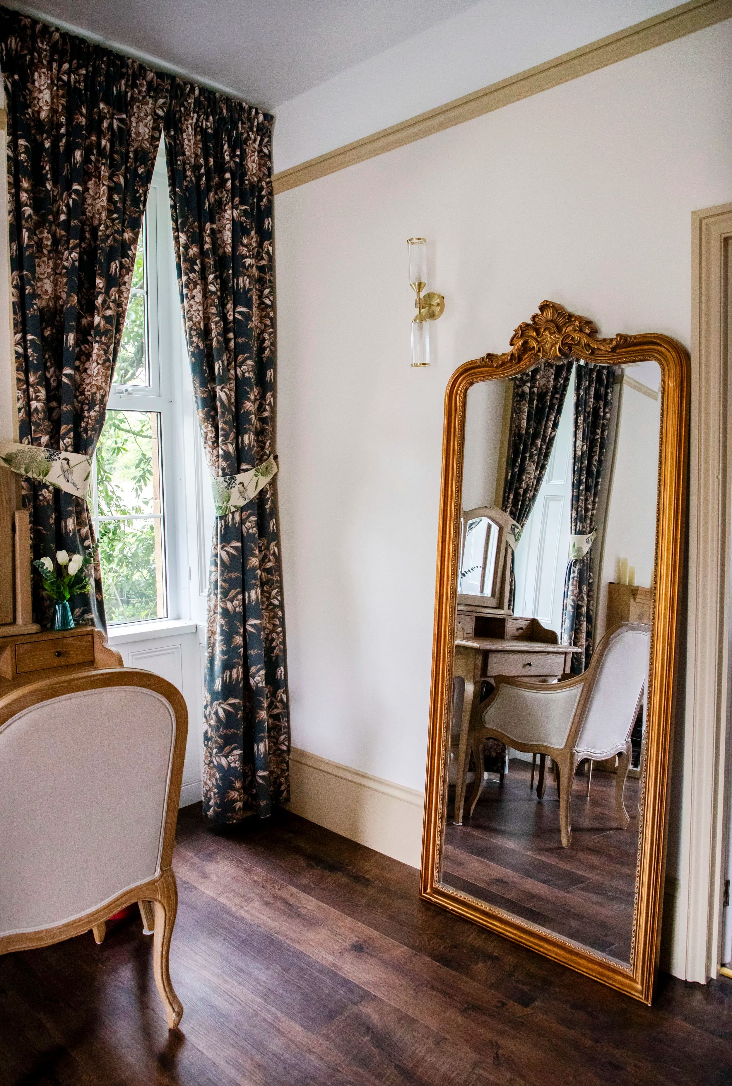 A guest room with a gilt mirror and floral curtains
