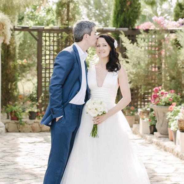 A groom kissing his bride's forehead in a walled garden
