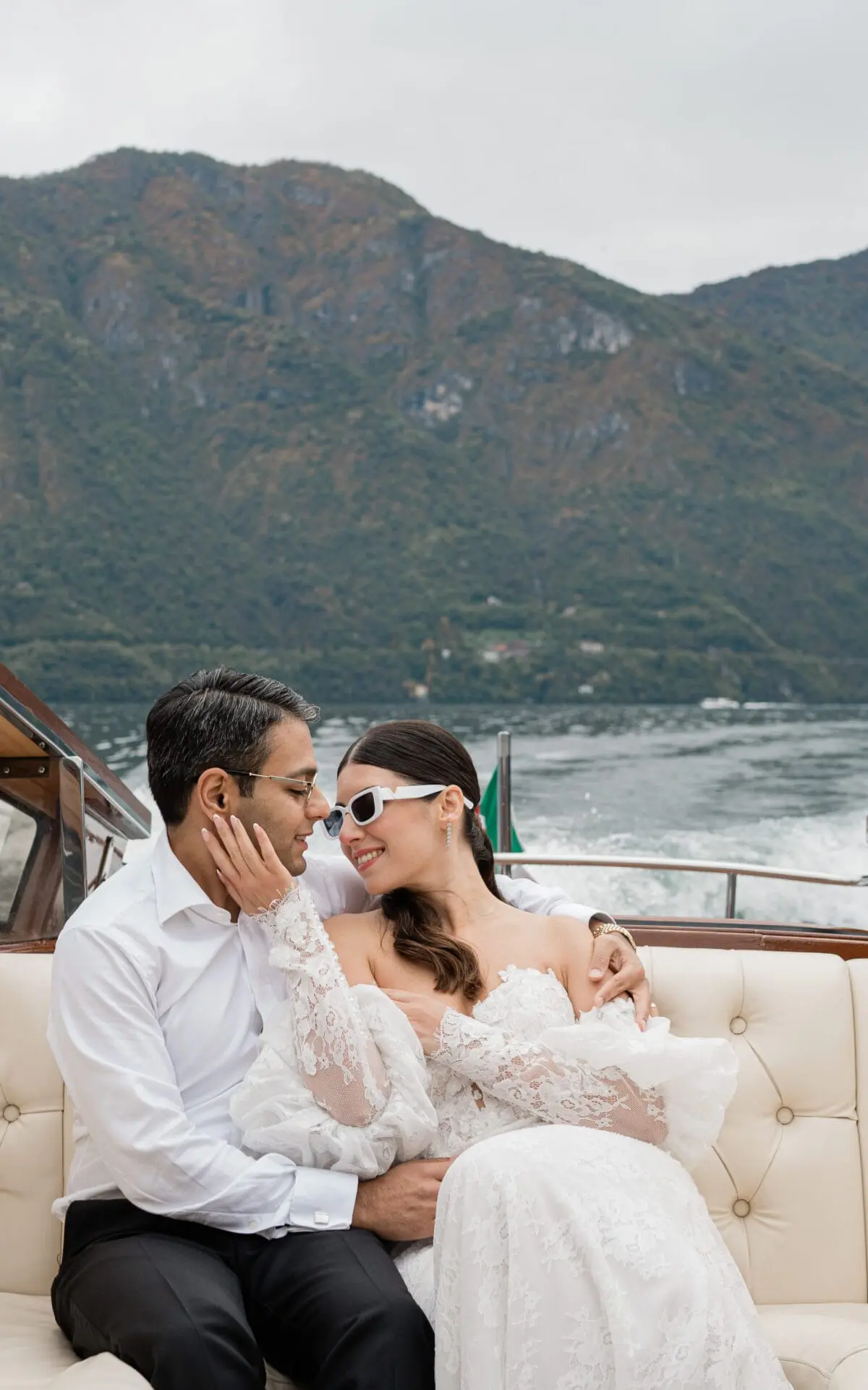 A couple aboard a wooden launch with mountains across the water
