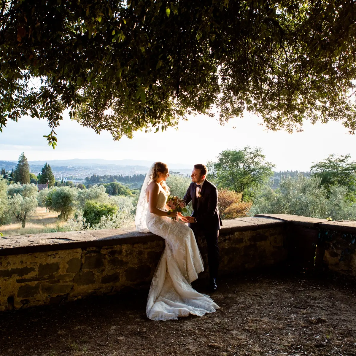 A couple under an olive tree on a stone terrace above Florence at sunset