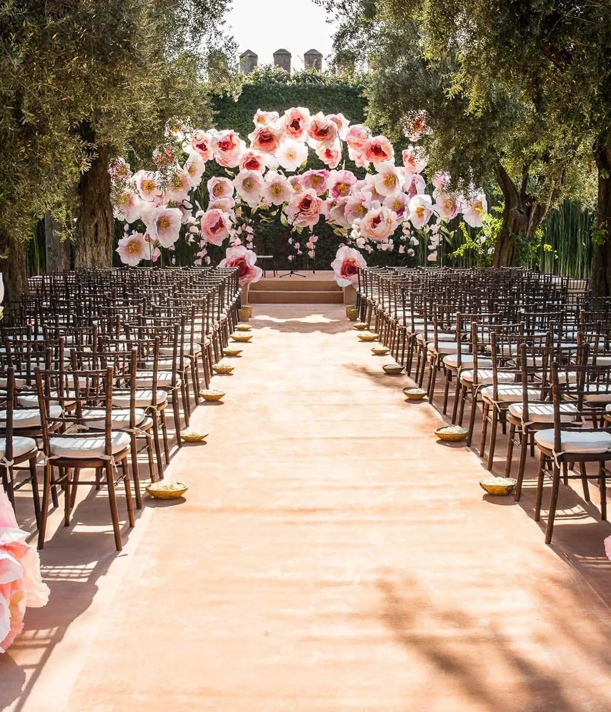 A rose-lined garden ceremony aisle set with chairs among the trees of the historic gardens, La Mamounia, Marrakech, Morocco