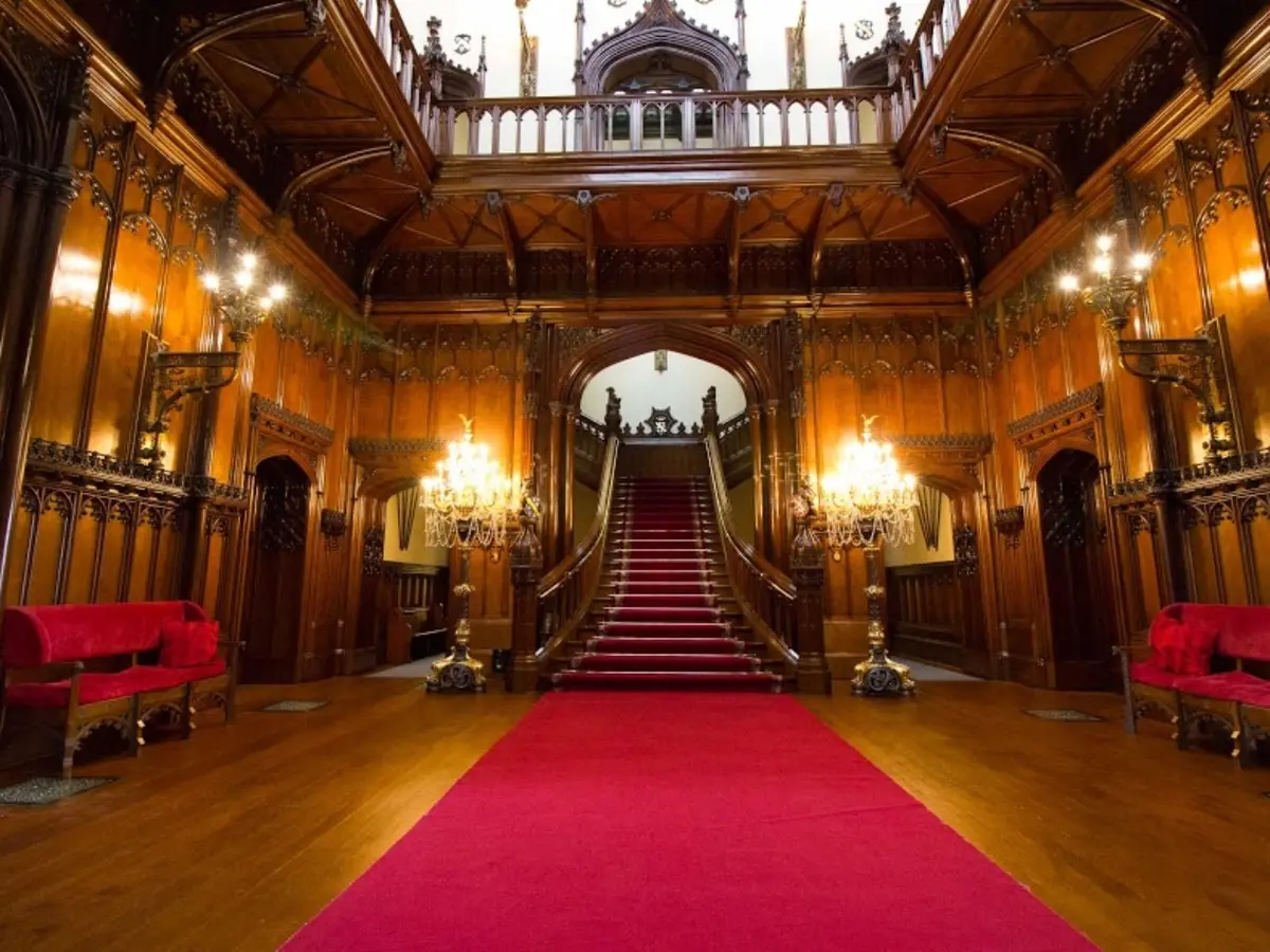 The Great Hall, its oak-panelled walls and grand red-carpeted staircase lit warm for the evening, Allerton Castle, Knaresborough, England