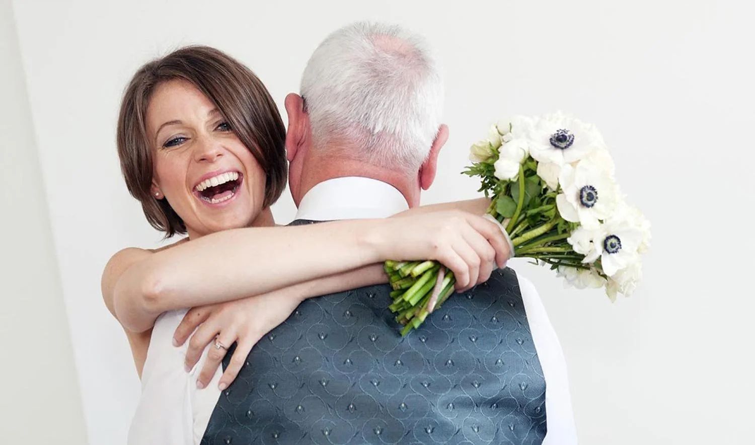 A bride embracing her father, an anemone bouquet between them, Dartmouth House