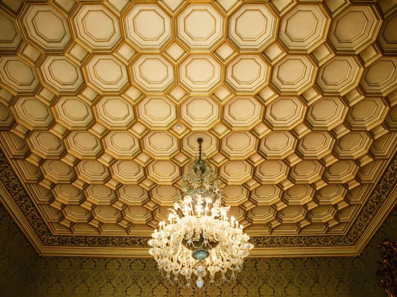 A gilded, coffered ceiling with a chandelier at its centre