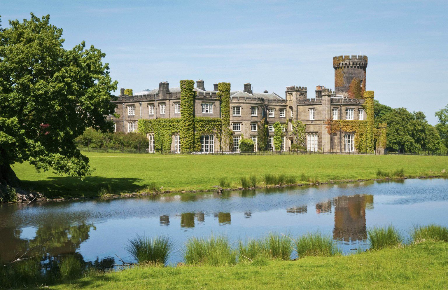 The castle mirrored in the still water of the estate lake, its tower reflected, Swinton Park, Masham, England