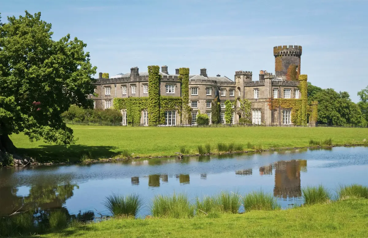 The castle mirrored in the still water of the estate lake, its tower reflected, Swinton Park, Masham, England