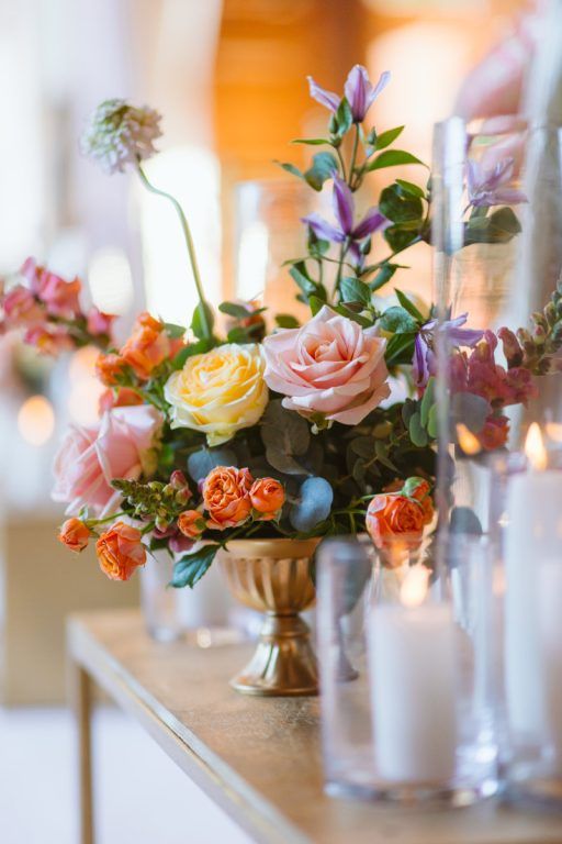 A reception centrepiece in a gold urn, pink and peach rose among candlelight