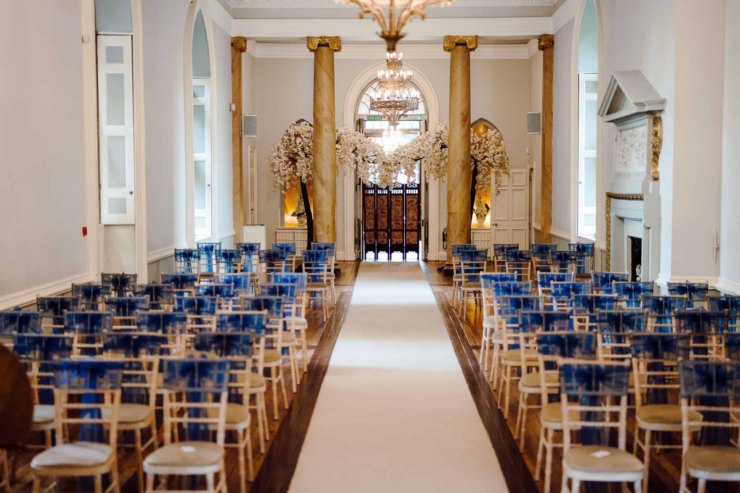 A ceremony in the columned Ballroom, blue chairs set to the arched entrance doors beneath the chandelier