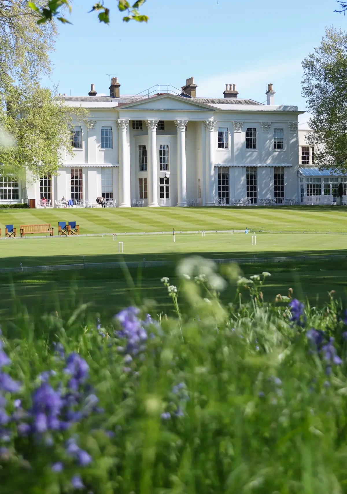 The clubhouse beyond the croquet lawn, with spring bluebells