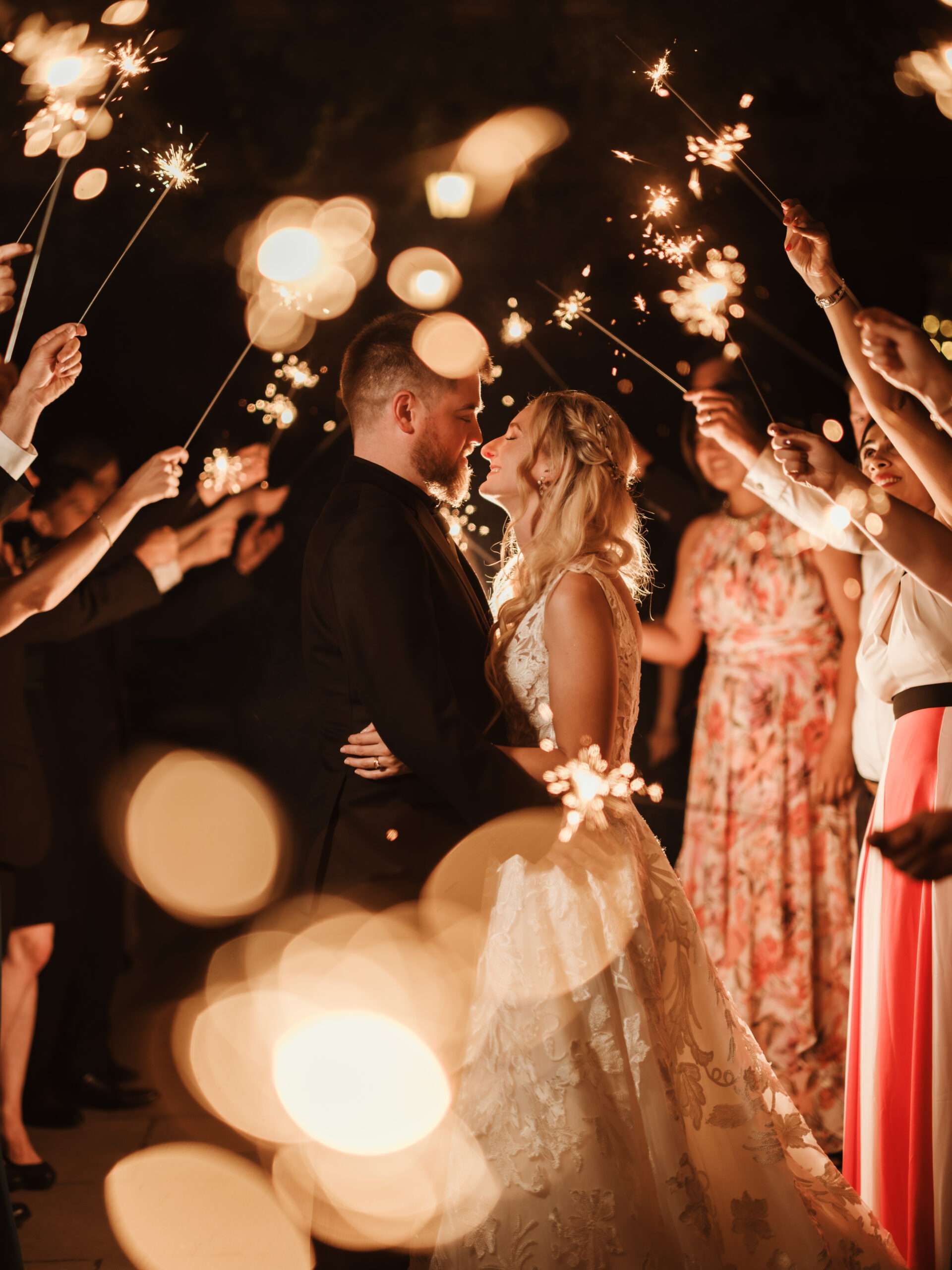 A couple kissing amid guests holding sparklers after dark