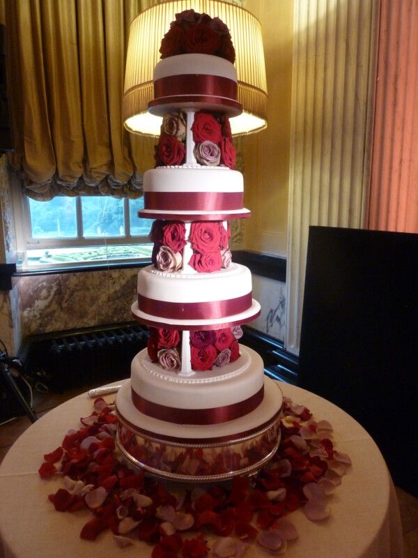 A five-tier wedding cake, dressed in red roses and petals
