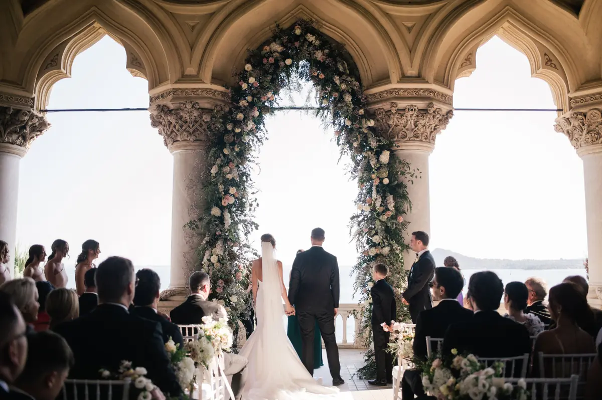 A kiss on the bow of a wooden boat, Isola del Garda's neo-Gothic villa rising behind, Lake Garda