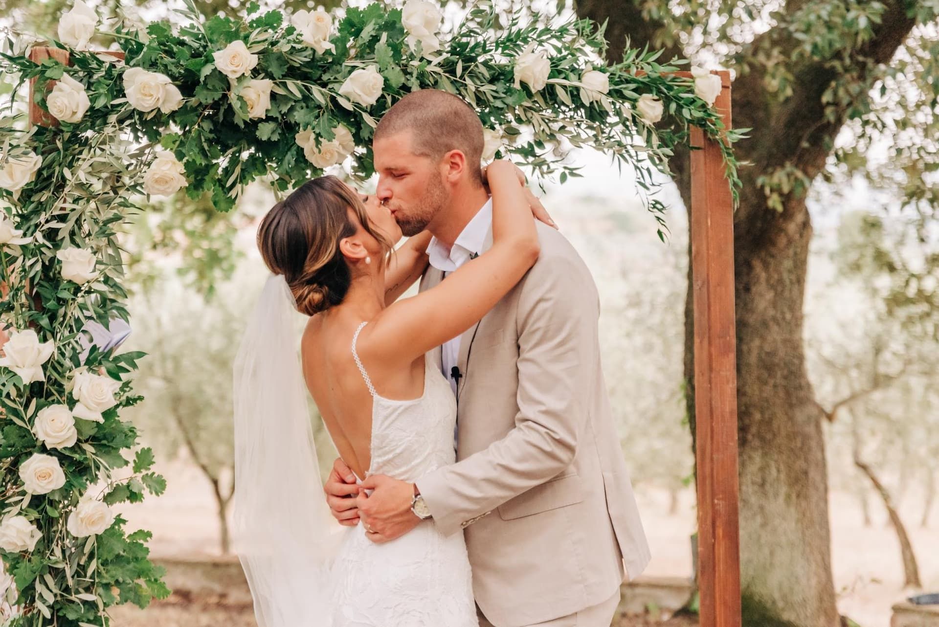 A kiss under an arch of white roses and olive