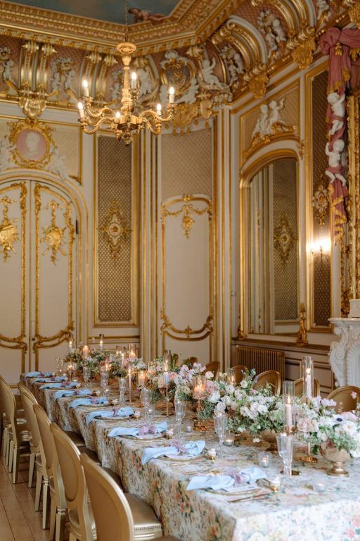 A long banquet table dressed with candles and florals beneath the gilded Gold Room ceiling