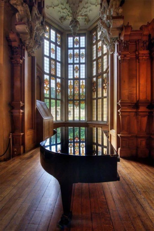 A grand piano framed by a stone-mullioned bay window overlooking the gardens