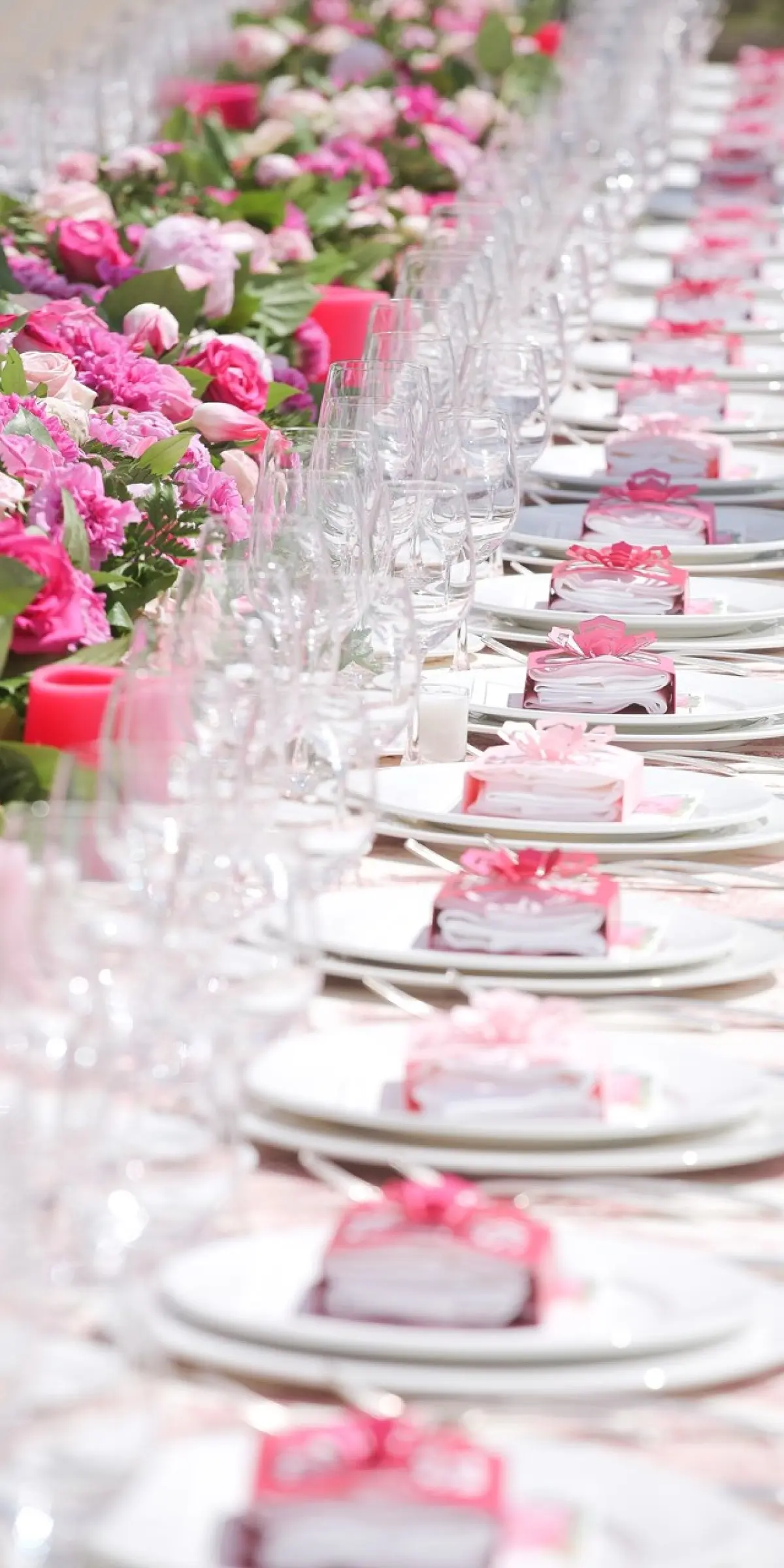 A solid runner of pink roses down a wedding table with crystal at every place