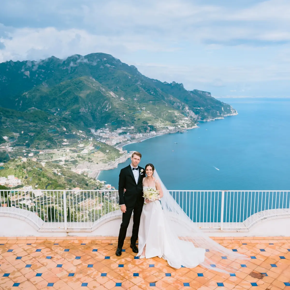 A couple on a clifftop balcony above Ravello, the Amalfi Coast spread out behind them
