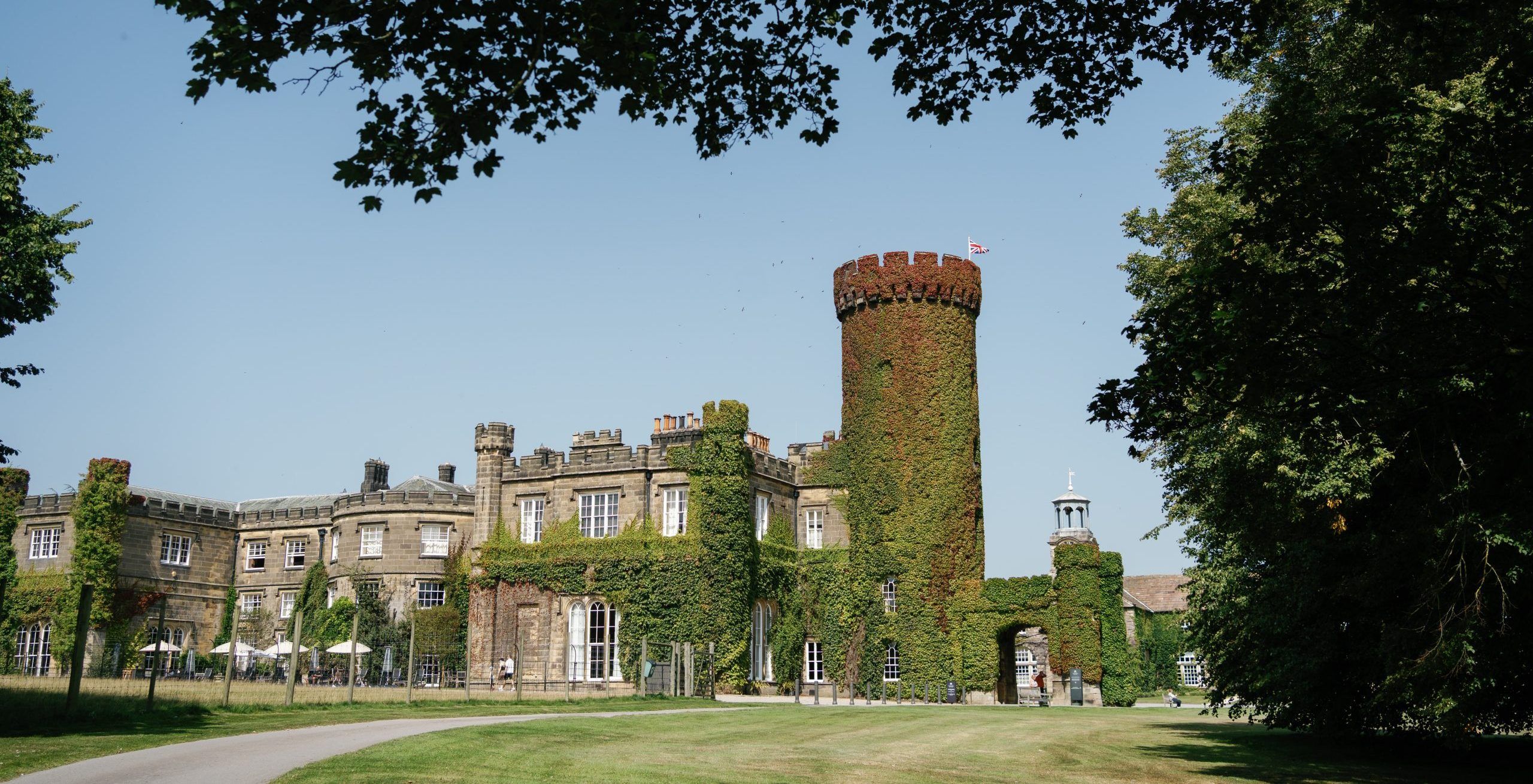 The castle exterior, the ivy-clad round tower rising above the castellated wings on a summer day, Swinton Park, Masham, England