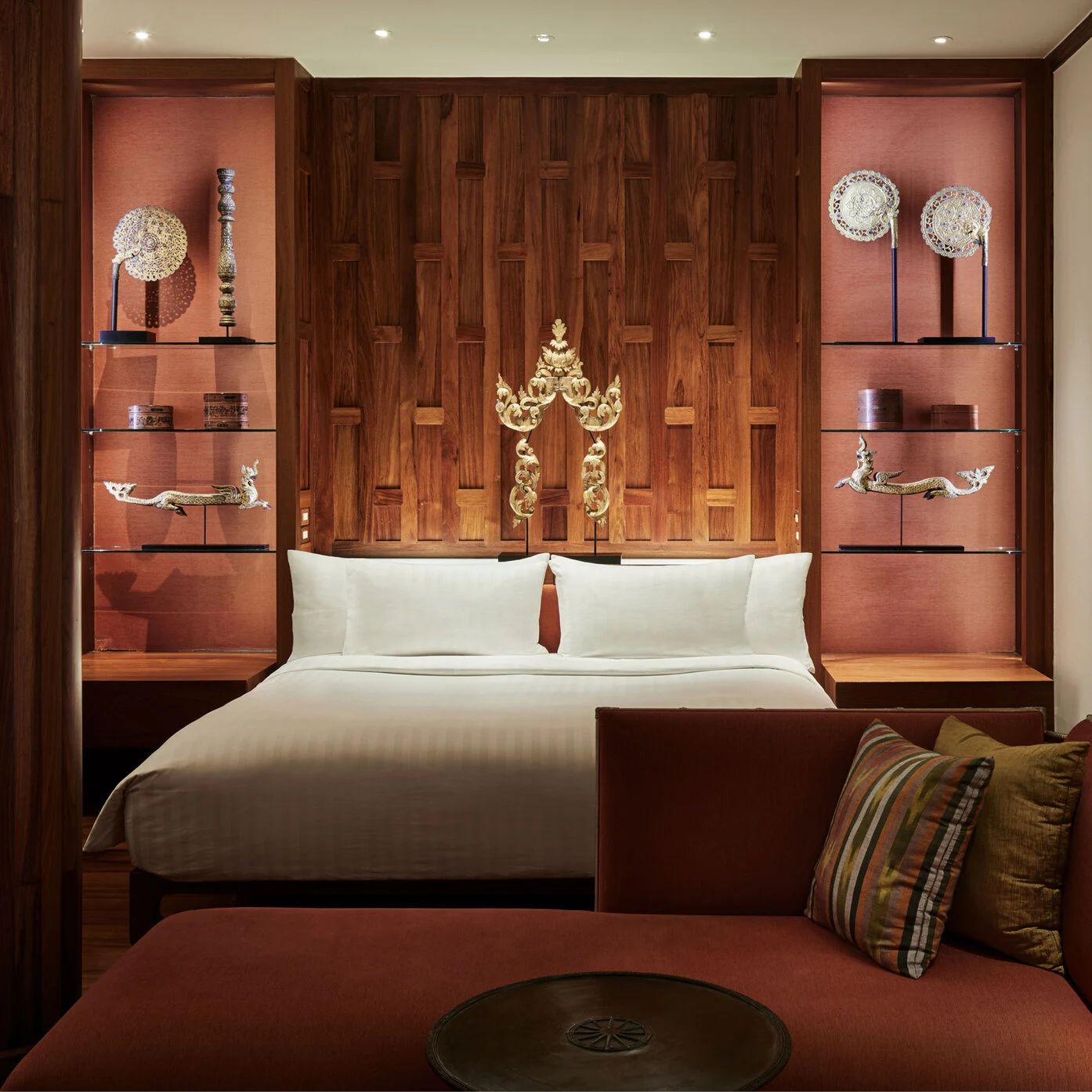 A bedroom at Amanpuri, teak panelling and a carved gold Thai ornament above the bed