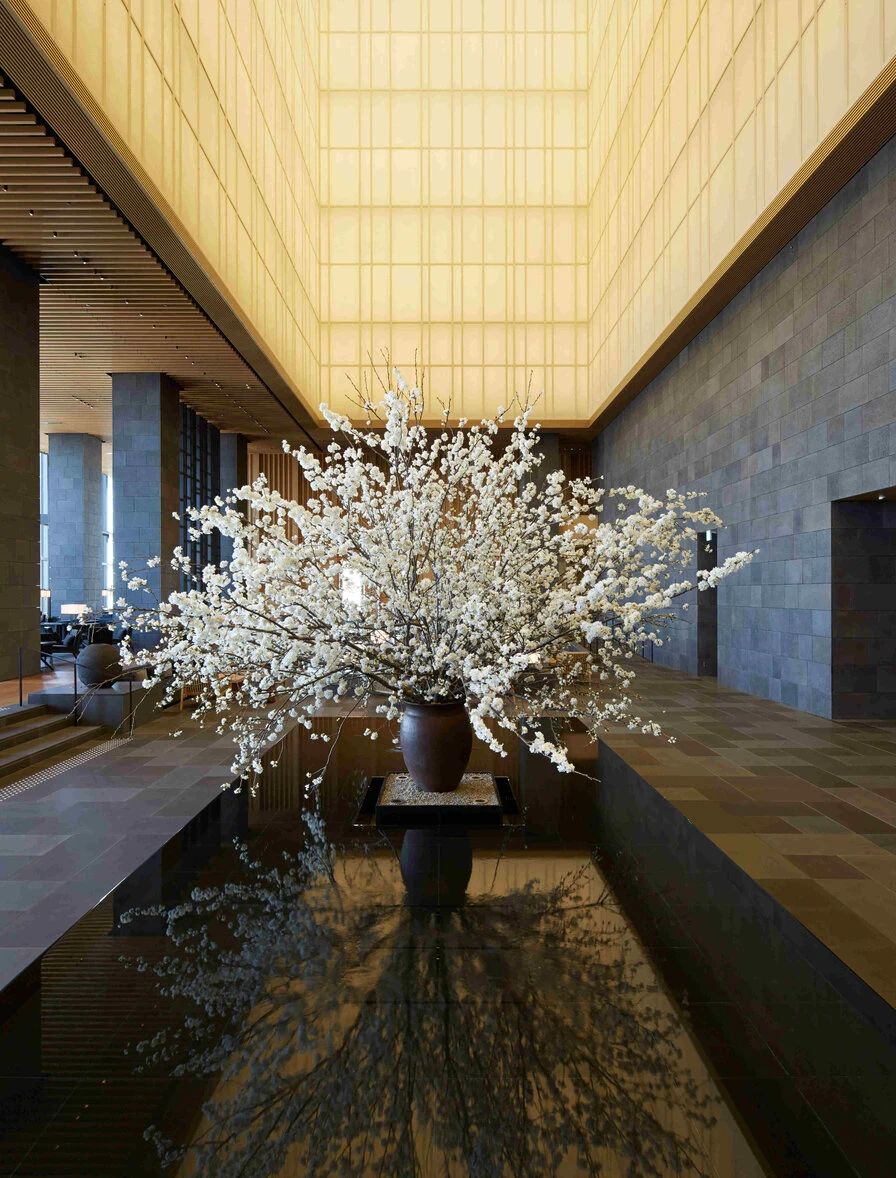 The soaring stone lobby of Aman Tokyo, with a reflecting pool and seasonal blossom arrangement